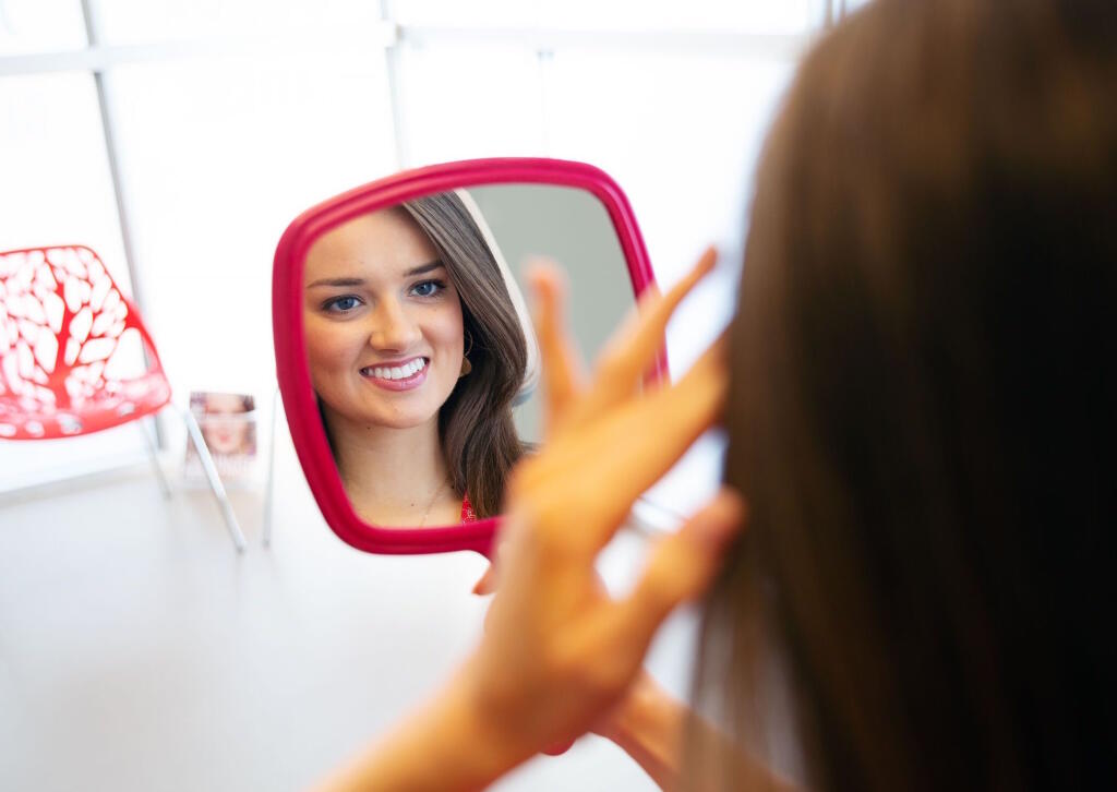 Reflection of a woman smiling into hand-held mirror