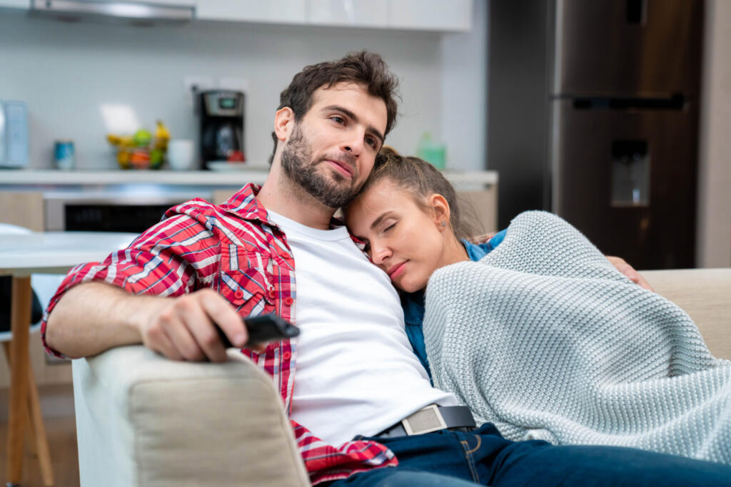 Couple on couch, woman under a blanket and resting against man