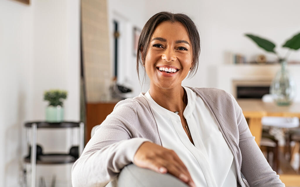 Woman sitting on couch in a house smiling at camera