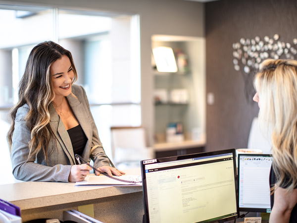 Woman smiling at office receptionist and filling out paperwork