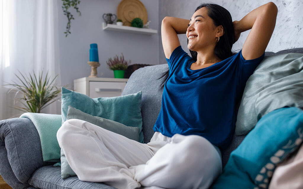 Woman sitting on a couch smiling with hands clasped behind head