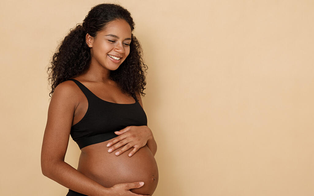 Pregnant woman in sports bra holding stomach and smiling