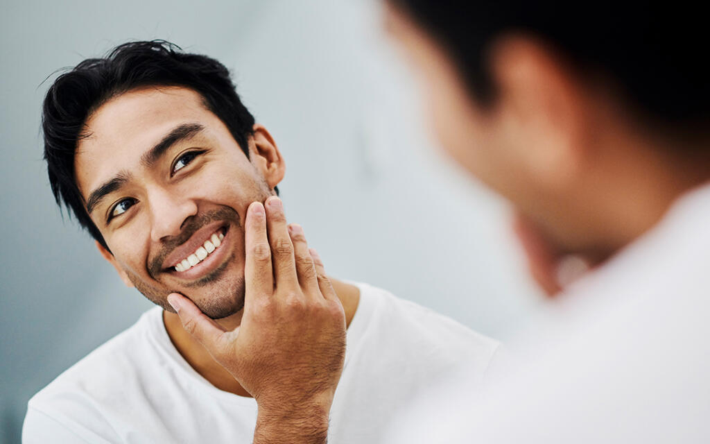 Man looking in mirror smiling and touching chin