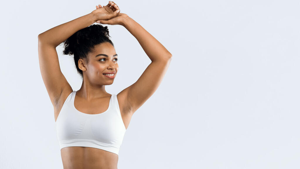 Woman in sports bra standing with arms above head and hands touching